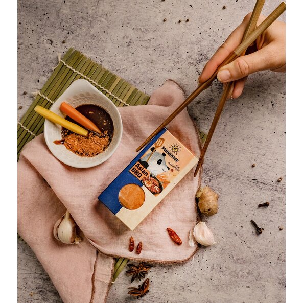 Asian BBQ spice pack next to a bowl with marinade, ginger, garlic and chopsticks on a light Asian-decorated background.