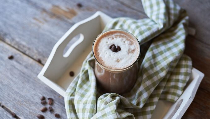 Nudelholz Kaffee Smoothie | © SONNENTOR Auf dem Foto sieht man ein Glas Kaffee Smoothie. Es steht auf einem weißen Tablett mit einem grün-weißem Tuch darauf. | © SONNENTOR